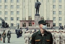 man in green and brown camouflage uniform standing near people in front of building during daytime