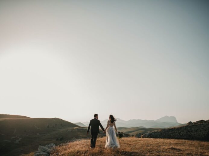 a bride and groom walking on a hill