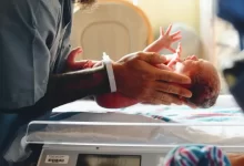 person wearing gray shirt putting baby on scale