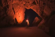 man holding red light flare inside cave
