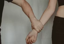 Unrecognizable aggressive man seizing hand of vulnerable helpless woman while standing on white background during domestic violence in light room