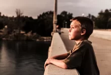 selective focus photo of boy at the bridge near body of water