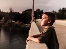 selective focus photo of boy at the bridge near body of water