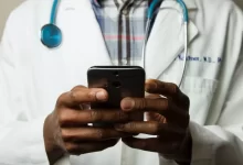 person wearing lavatory gown with green stethoscope on neck using phone while standing