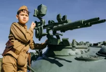 a boy in a uniform standing next to a tank