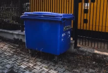 blue trash bin beside yellow metal fence