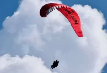 person riding on red and white parachute under white clouds and blue sky during daytime