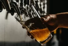 person pouring brown liquid on clear drinking glass