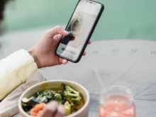 Crop unrecognizable female blogger touching screen on cellphone above street cafe table with healthy food and smoothie