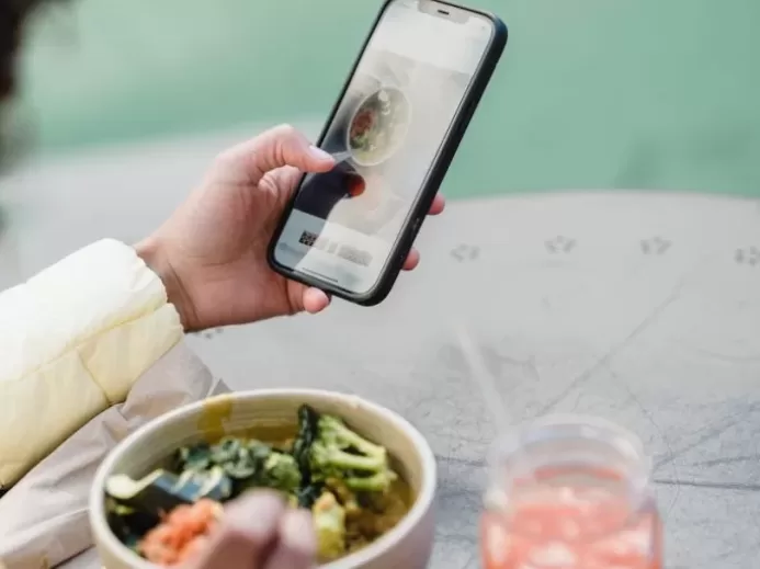 Crop unrecognizable female blogger touching screen on cellphone above street cafe table with healthy food and smoothie