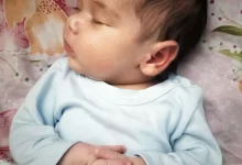 baby in blue long sleeve shirt lying on pink and white floral textile