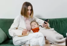 Woman Using Phone with Sick Child Sleeping in her Arms