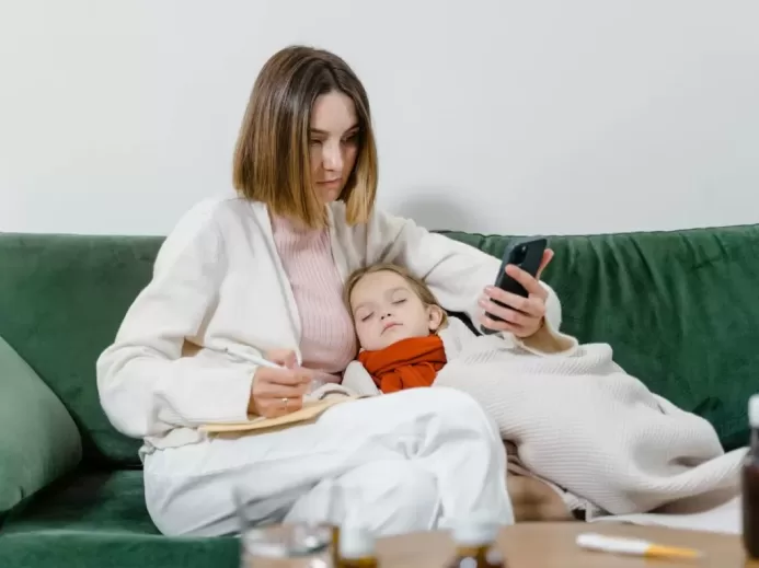 Woman Using Phone with Sick Child Sleeping in her Arms