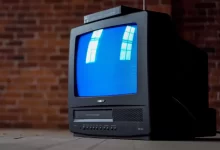 gray crt tv turned on beside brown brick wall