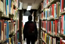 man with backpack beside a books