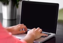 person wearing pink shirt typing on gray laptop computer on desk