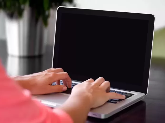 person wearing pink shirt typing on gray laptop computer on desk