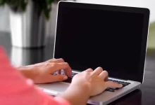 person wearing pink shirt typing on gray laptop computer on desk