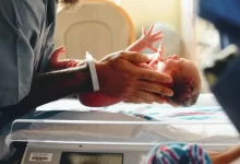 person wearing gray shirt putting baby on scale