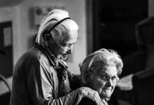 greyscale photo of woman standing behind woman sitting on chair