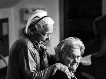 greyscale photo of woman standing behind woman sitting on chair