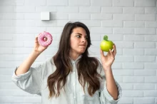 Žena rozhodující se, jestli sní jablko nebo donut.