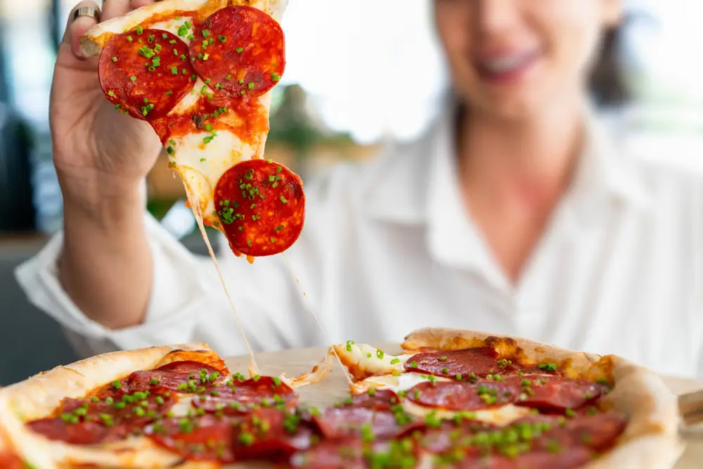 Žena drží v ruce salámovou pizzu. 
