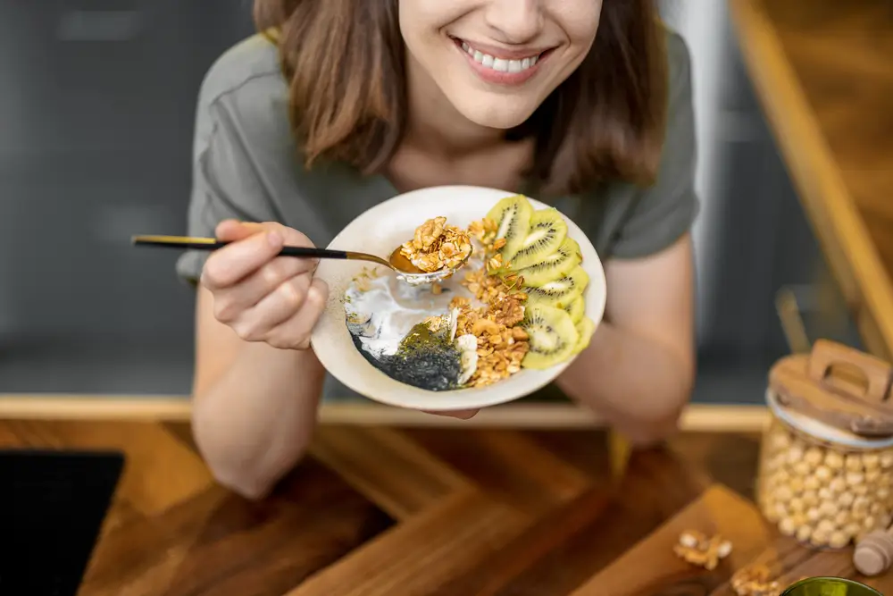 shutterstock_1938080527 - Pravda24 Žena drží v ruce talíř, který je plný ovoce, jogurtu a ořechů.