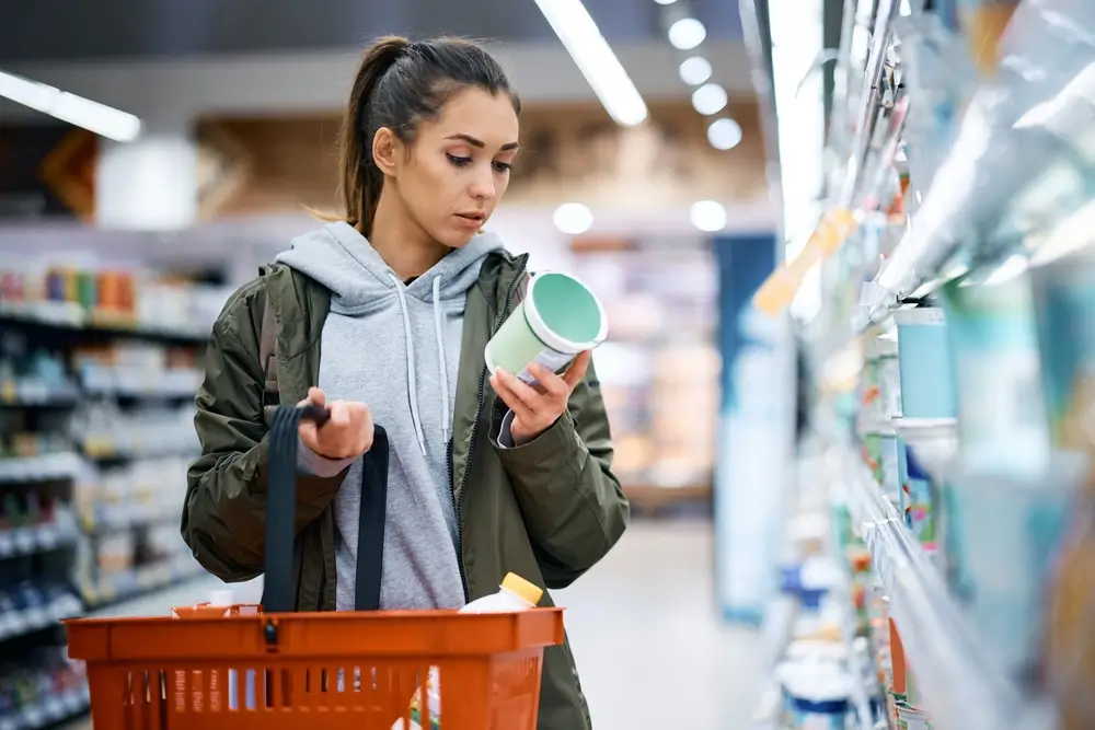 shutterstock_2136267049 - Pravda24 Žena drží v ruce jogurt a prohlíží si jej.