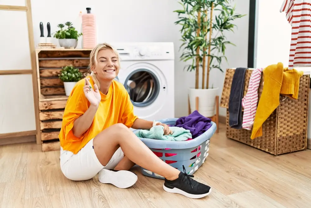 shutterstock_2238210843 - Pravda24 Žena sedí před pračkou a usmívá se.