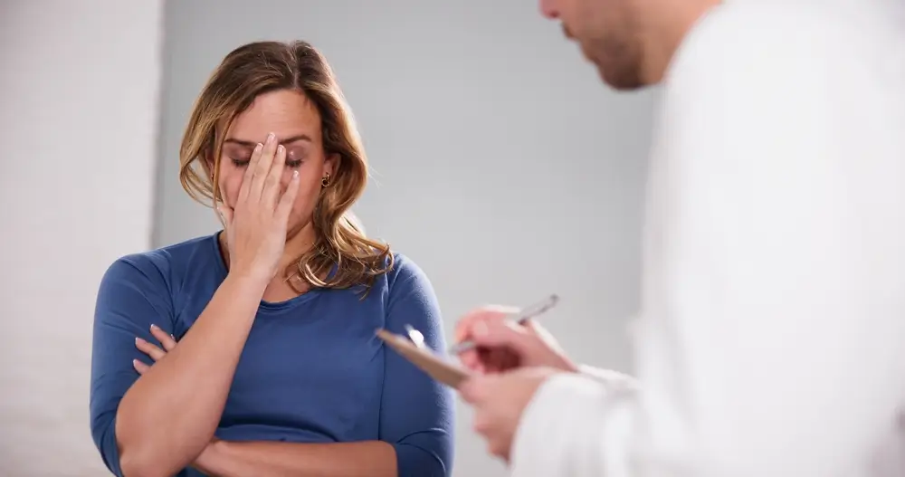 shutterstock_2255119901 - Pravda24 Žena se zoufale drží za čelo. Lékař na ni hledí a něco si zapisuje.