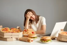 Žena sedí u stolu, který je plný nezdravých potravin.