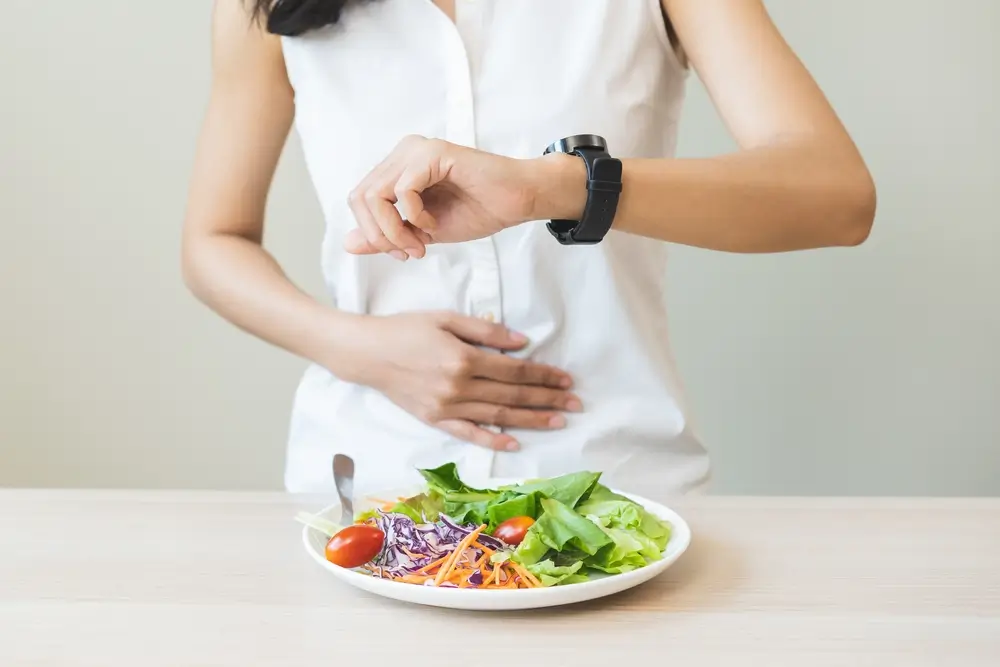 shutterstock_2341509165 - Pravda24 Žena má na stole talíř se zeleninou a dívá se na hodinky.