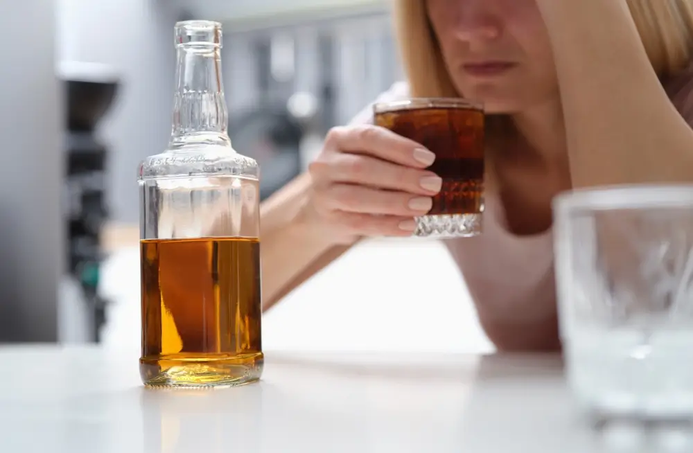 shutterstock_2361021407 - Pravda24 Žena se drží za hlavu, zatímco pije alkohol.