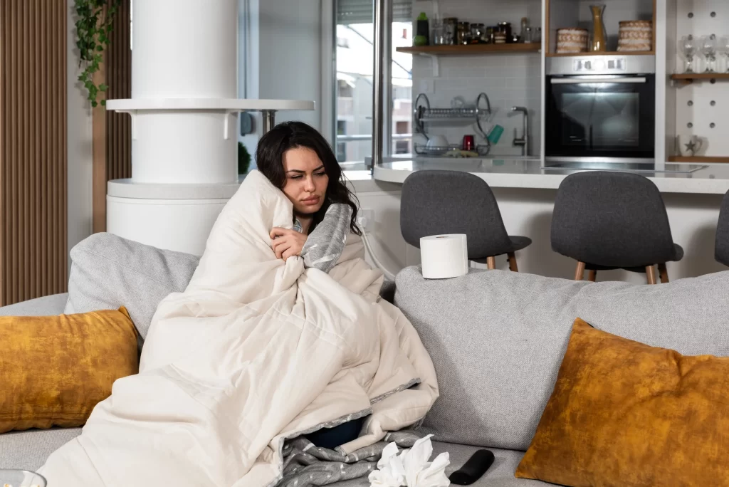 Při nemoci raději zůstávejte doma. Zdroj: Shutterstock - Pravda24 Nemocná žena sedící na gauči.