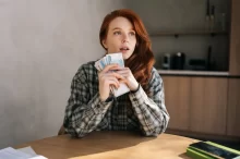 Žena sedí u stolu a drží v ruce peníze.