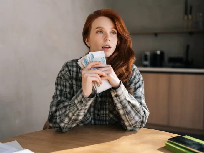 Žena sedí u stolu a drží v ruce peníze.