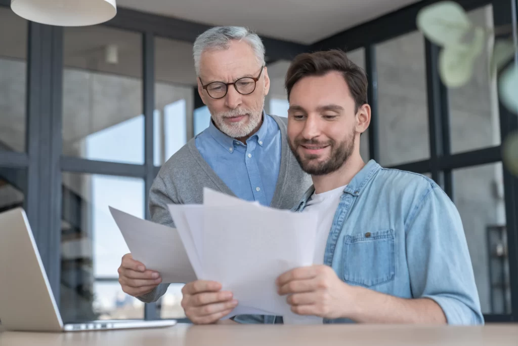 Peníze důchodcům nyní budou vyplaceny dříve. Zdroj: Shutterstock - Pravda24 Senior a mladší muž dívající se do papírů.
