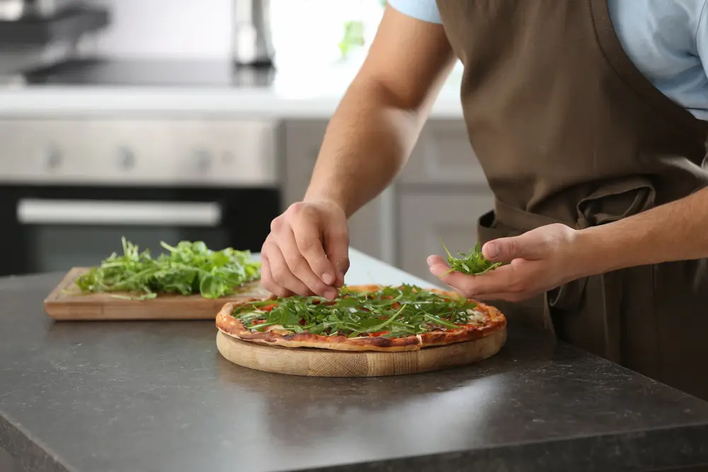 shutterstock_1306708423 - Pravda24 Muž připravuje pizzu s rukolou.