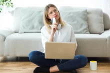 Žena drží v ruce kartu, má notebook na klíně a přemýšlí.