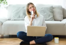 Žena drží v ruce kartu, má notebook na klíně a přemýšlí.