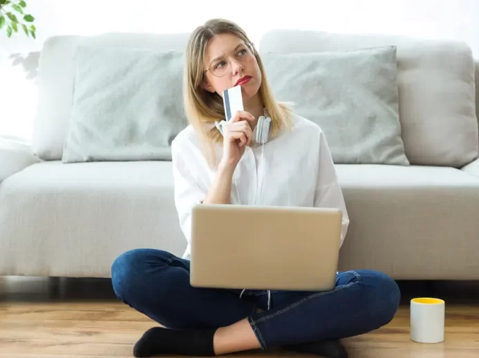 Žena drží v ruce kartu, má notebook na klíně a přemýšlí.