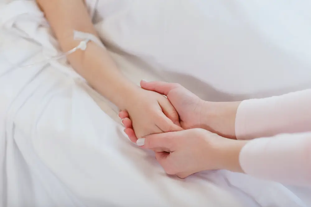 Žena drží z empatie svýma rukama ruku další ženy, která je na kapačkách. 