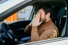 Muž sedí v autě a drží se za hlavu.