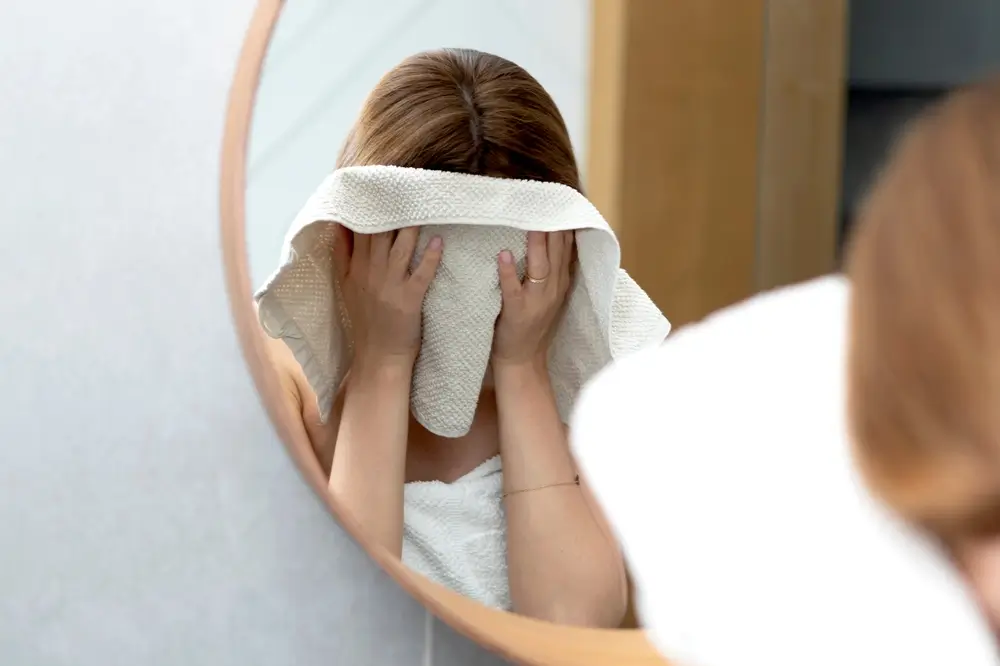 shutterstock_2297560339 - Pravda24 Žena si utírá obličej do ručníku.