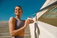 Žena má zvednutou ruku s hodinkami a usmívá se.