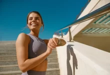 Žena má zvednutou ruku s hodinkami a usmívá se.