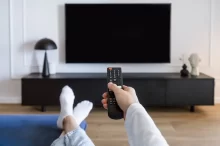 Žena leží na pohovce a zapíná TV.