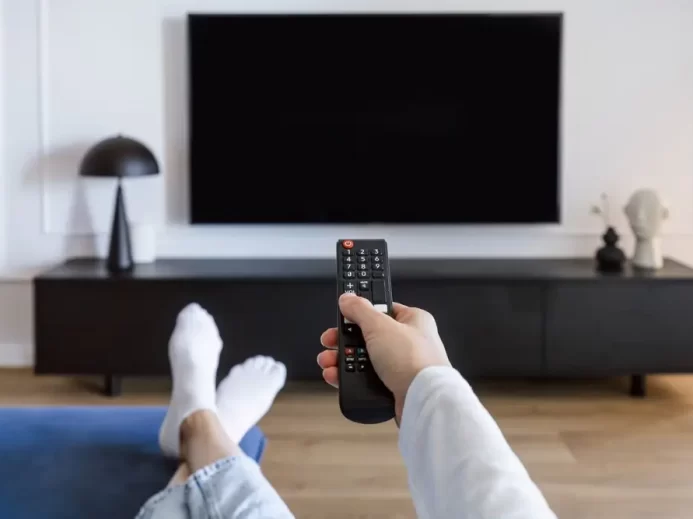 Žena leží na pohovce a zapíná TV.