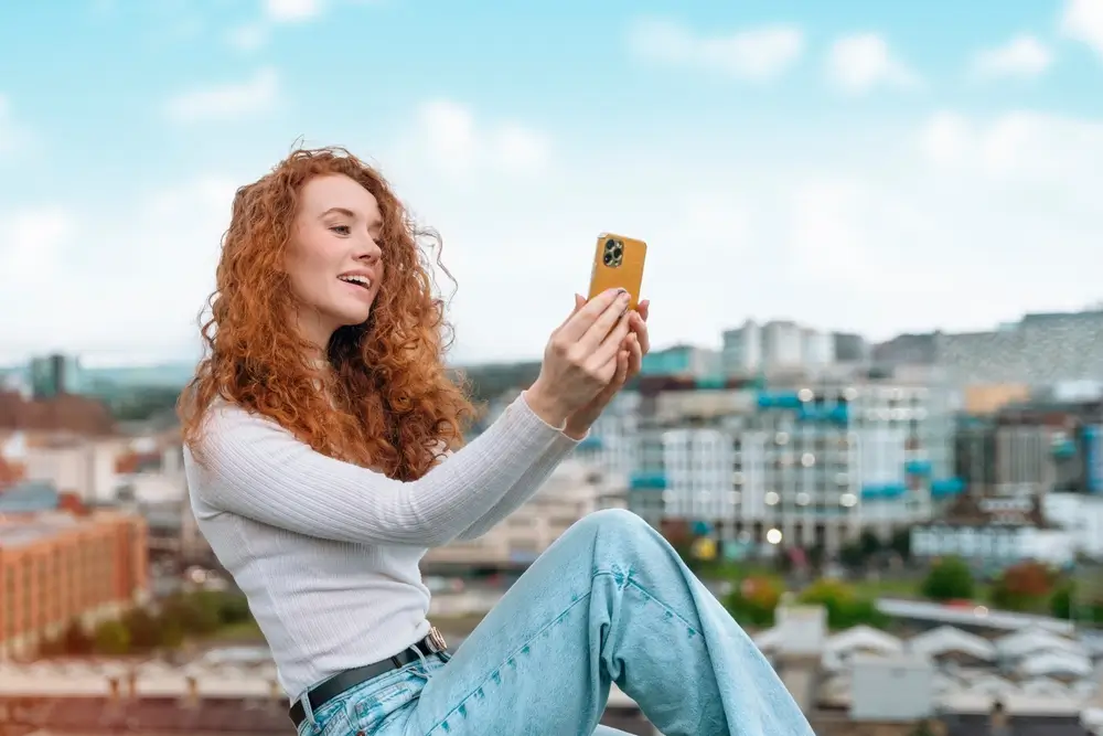 shutterstock_2459124721 - Pravda24 Žena, která má zrzavé vlasy, drží v rukou telefon.